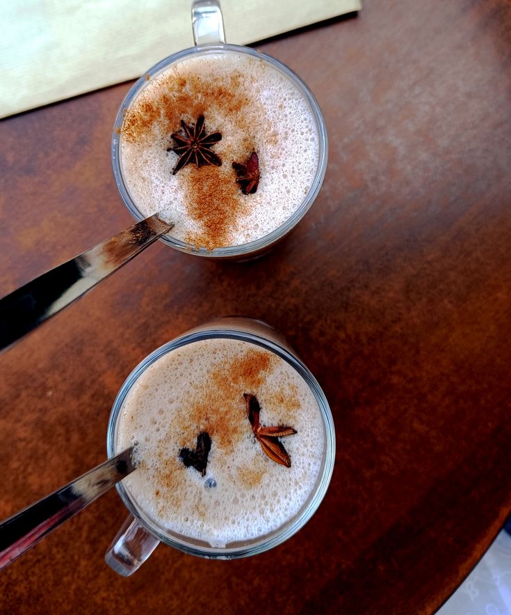 Two glass coffee cups with foam and star anise on wooden table, overhead view