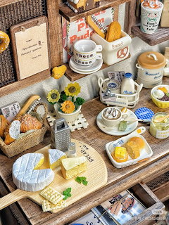 Overhead view of miniature cafe items with coffee cups, desserts, sunflowers, and decorative accessories on wood display