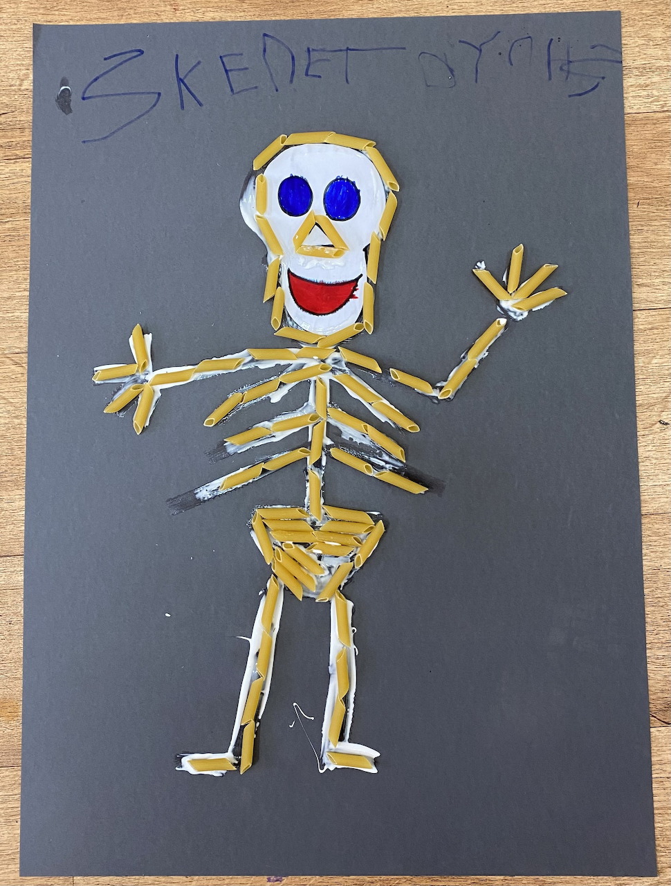 Child's painted skeleton with yellow bones, blue eyes and red smile on dark background paper