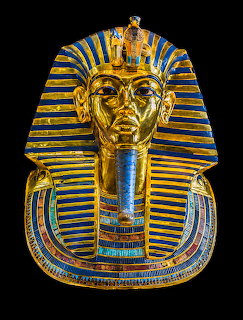 Golden funerary mask of Tutankhamun with blue and gold striped nemes headdress on black background