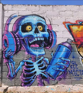 Colorful graffiti mural of a blue skeleton wearing headphones painted on a concrete wall
