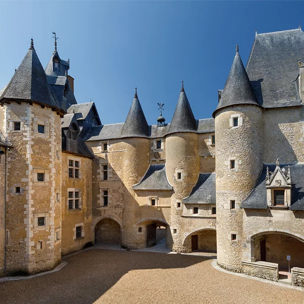 Stone castle courtyard with round towers and conical roofs under a clear blue sky