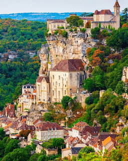 Historic village of Rocamadour perched on cliff with church and buildings cascading down stone face above green valley