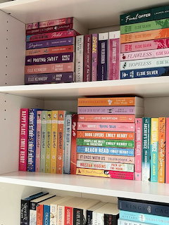 White bookshelf with colorful paperback books arranged in rainbow order across multiple shelves