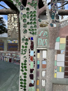 Mosaic-covered tree-like columns and walls with colorful glass and tile outdoors
