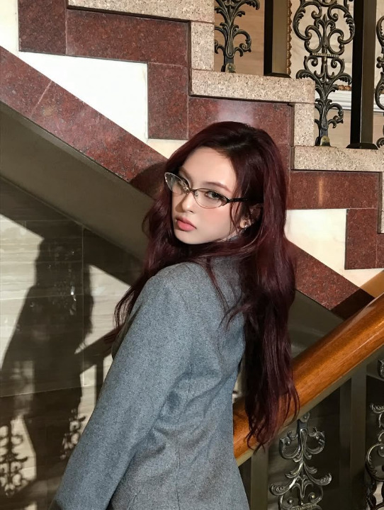 Young woman with burgundy hair and glasses looking over shoulder on ornate staircase