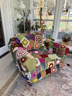 Armchair draped in colorful crocheted granny square blankets in a bright indoor room