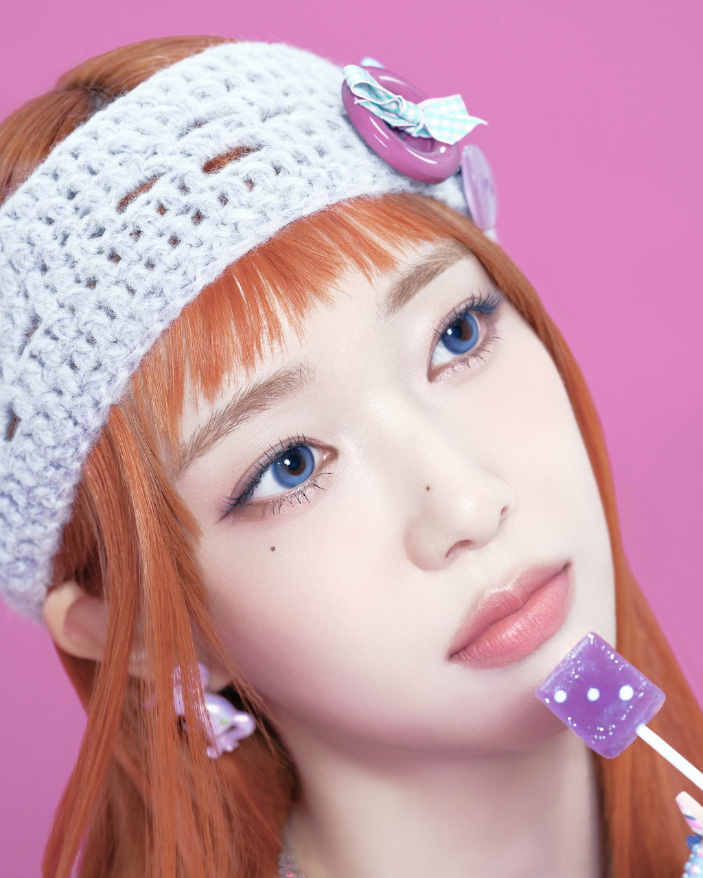 Portrait of young woman with orange hair wearing white knit hat against pink background