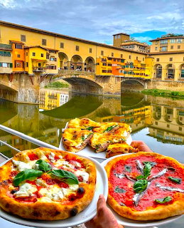 Two pizzas held in front of Ponte Vecchio bridge over the Arno River in Florence, Italy