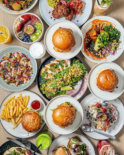 Overhead flatlay of various restaurant meals on white plates including burgers, salads, and sides