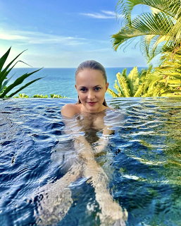 Woman in infinity pool with ocean and palm trees in background