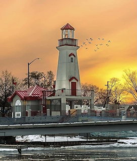 White lighthouse with red roofs beside a snowy shore at sunset