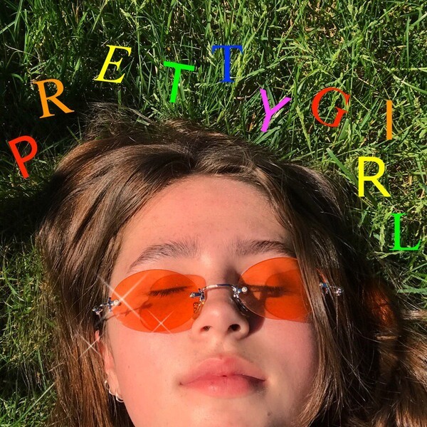 Young woman lying in grass wearing orange sunglasses with colorful letters overhead
