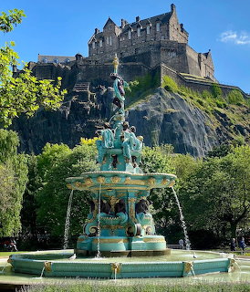 Turquoise Victorian fountain with Edinburgh Castle on rocky cliff behind under clear blue sky