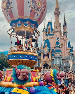 Disney parade float with cartoon characters in front of iconic blue and white castle with crowds watching