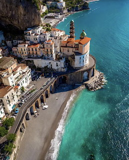 Aerial view of an Italian coastal town with a domed church, cliffside buildings, and turquoise sea