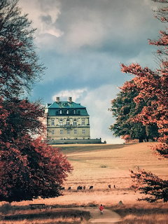 Three-story historical lodge building framed by colorful autumn trees under dramatic cloudy sky