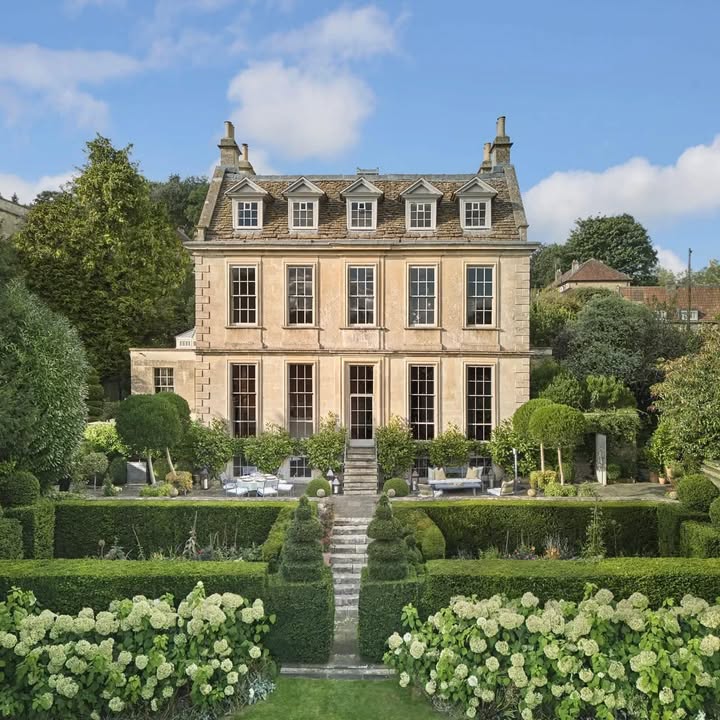 Georgian manor house with formal garden hedges, stone steps, and white flowering shrubs