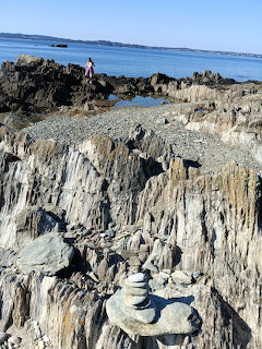 Jagged dark rock formations on a beach with a stone cairn and calm ocean in the background