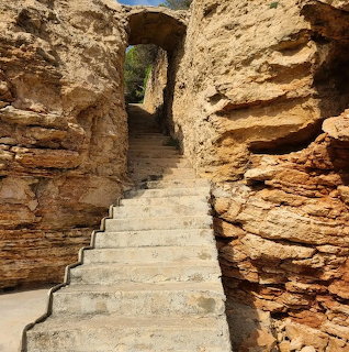 Stone stairs climbing through narrow canyon passage between orange-brown layered rock walls toward archway