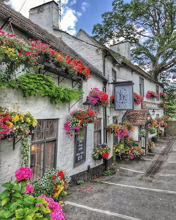 White-walled traditional English pub covered in colorful hanging flower baskets on a village street