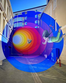 Colorful street mural with rainbow spiral and figure on blue building wall