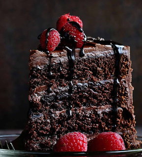 Slice of chocolate layer cake topped with raspberries and chocolate drizzle