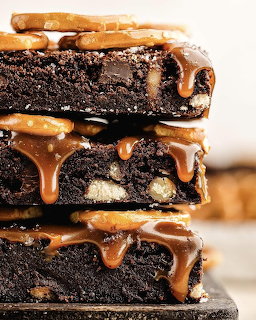 Stack of chocolate brownies topped with pretzels and dripping caramel sauce on a light background