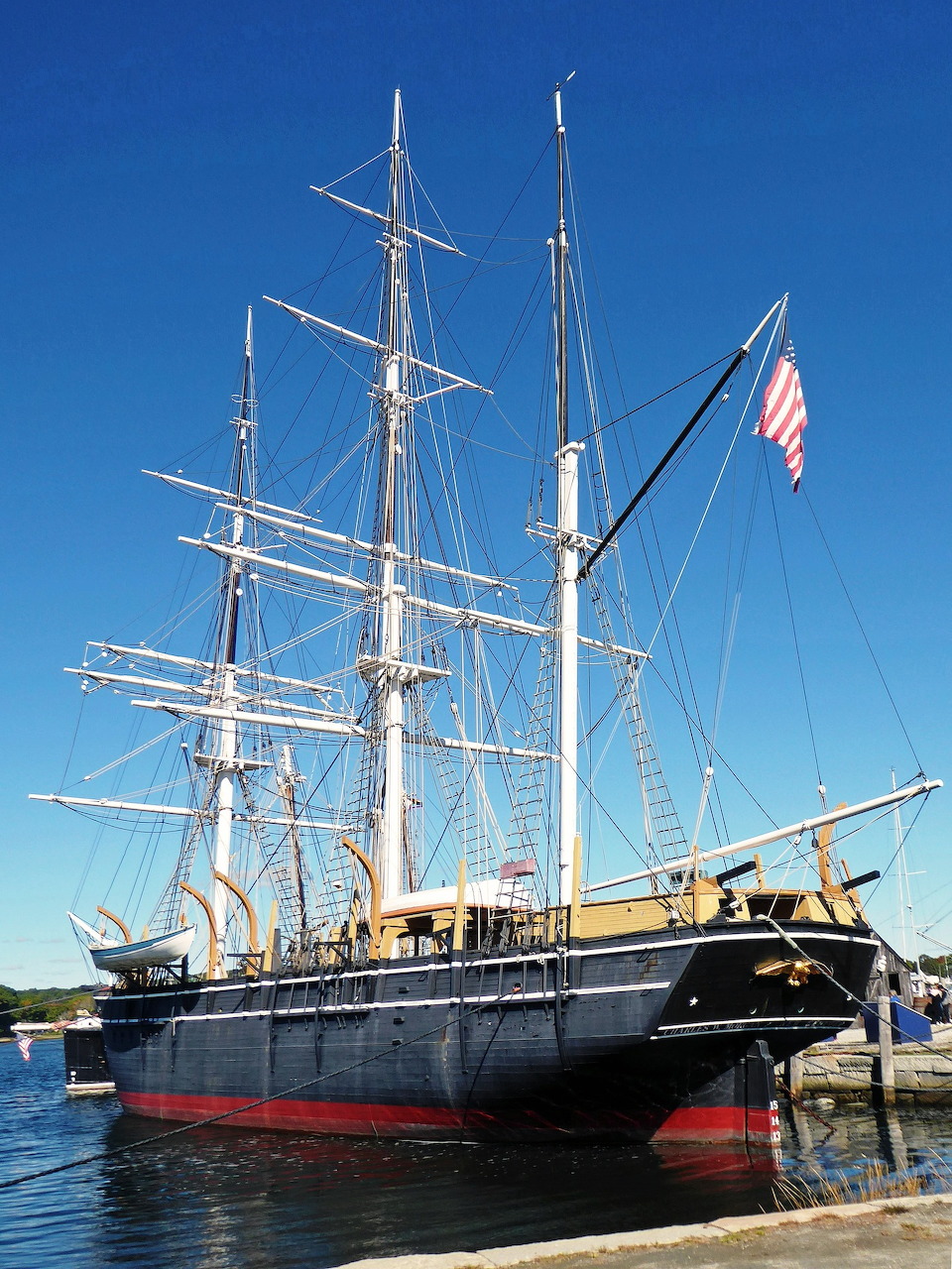 Historic tall ship Charles W. Morgan docked on calm water beneath a clear blue sky