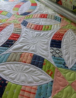 Close-up of a patchwork quilt with curved quilted leaf designs and colorful fabric strips