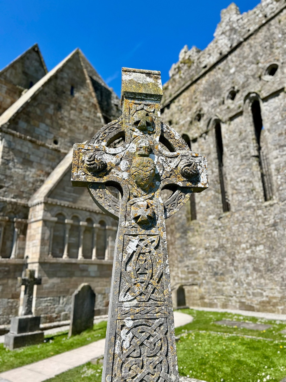 Stone Celtic cross in front of an old church building on a sunny day