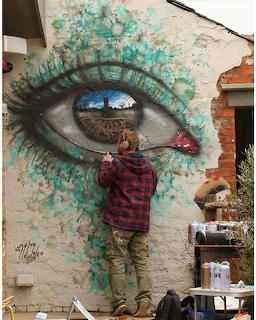 Person posing in front of large eye mural with turquoise paint splashes on building wall