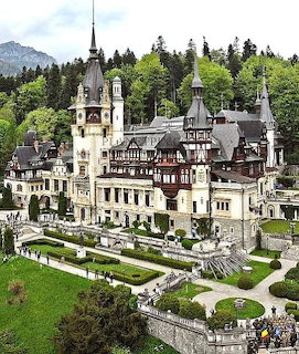 Peles Castle in Romania with ornate towers and terraced gardens surrounded by evergreen forest
