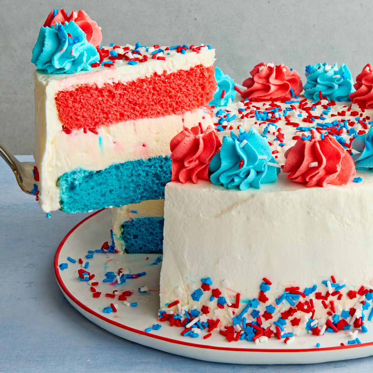 Red, white, and blue layer cake with white frosting, piped swirls, and patriotic sprinkles