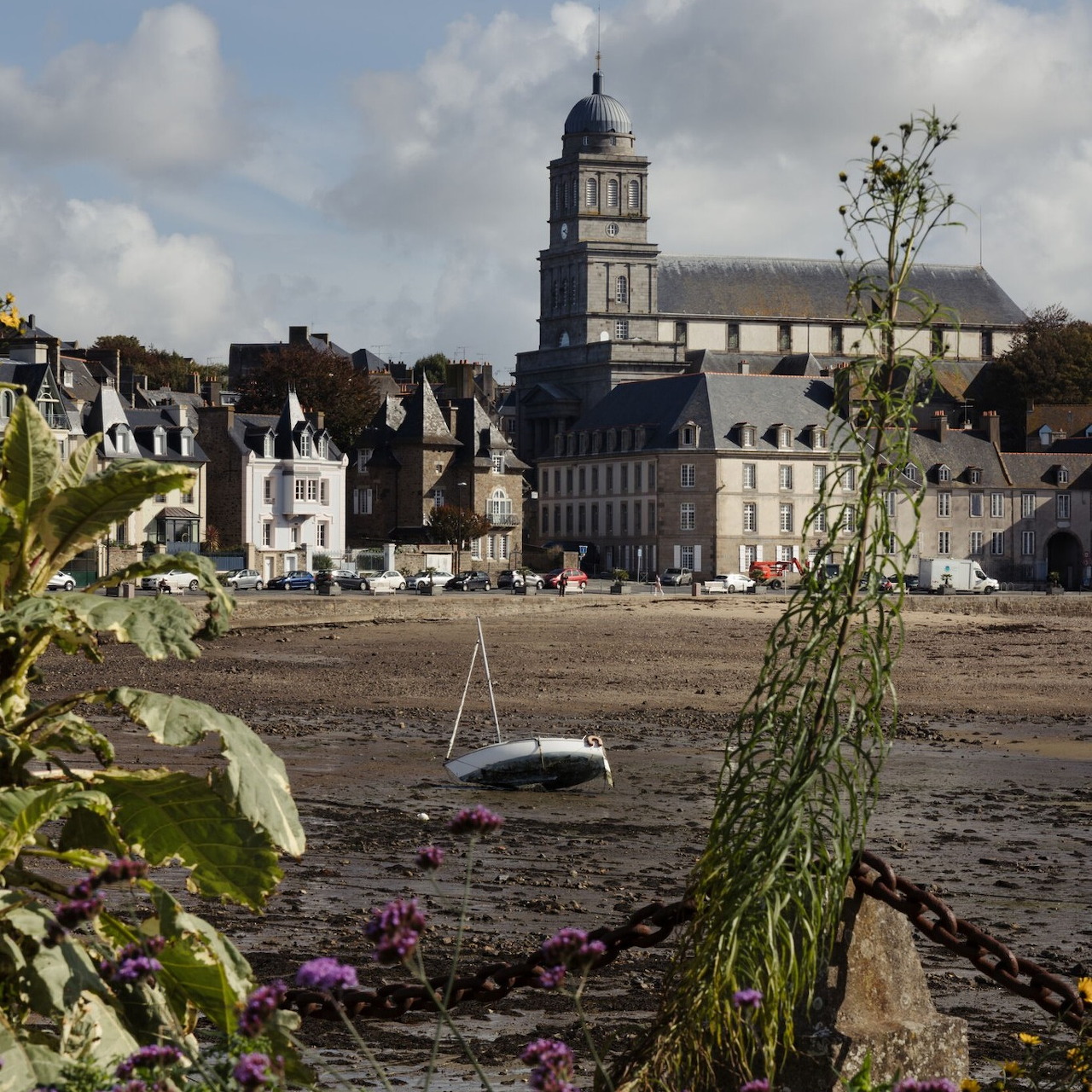 Saint-Malo harbor at low tide with beached boat, stone buildings and cathedral tower under cloudy sky