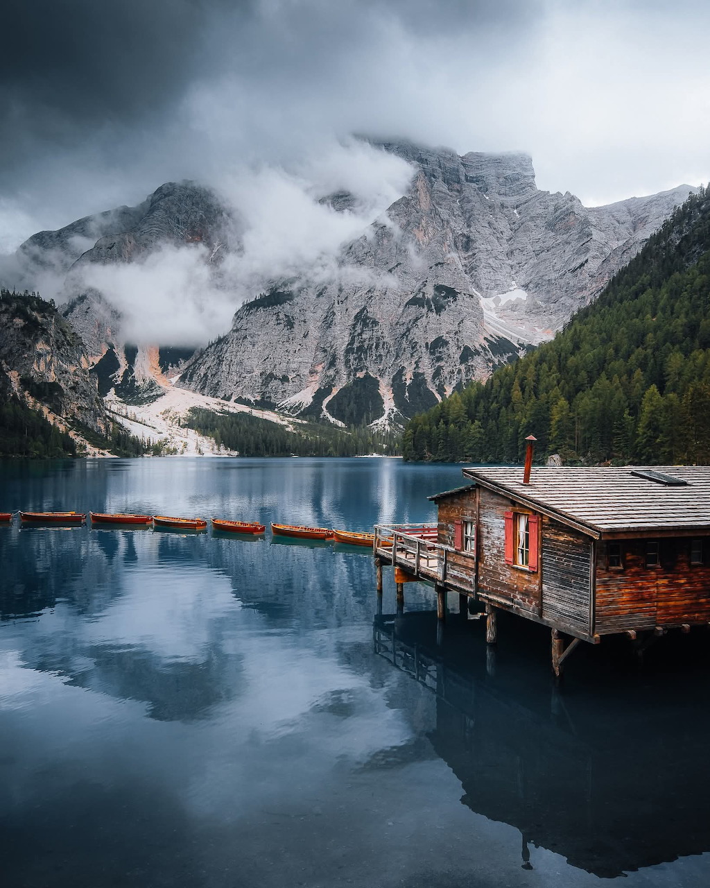 Wooden boathouse on a serene alpine lake with Dolomite mountains and pine forest reflected in calm water