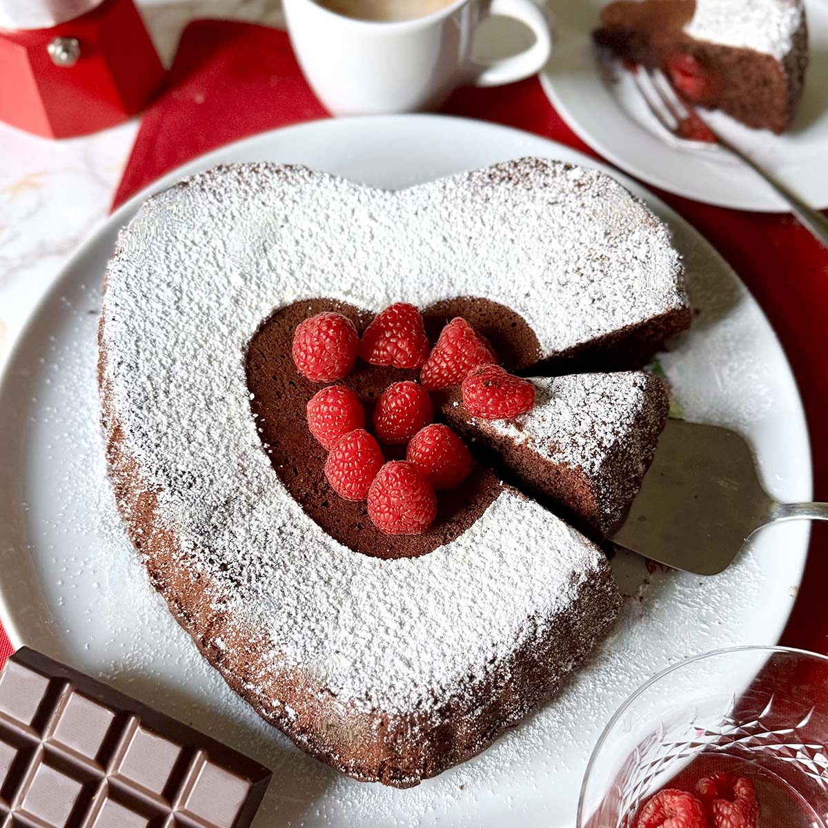 Heart-shaped chocolate cake with powdered sugar and raspberries on a white plate