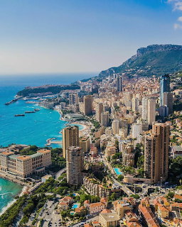 Aerial view of Monte Carlo Monaco with dense buildings, turquoise sea, and mountainous backdrop