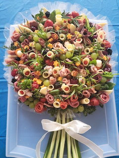 Charcuterie bouquet with rolled meats, cheese, olives and grapes arranged like flowers on a blue platter