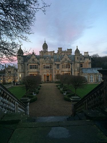 Grand historic manor castle at dusk with symmetrical garden path and twilight sky