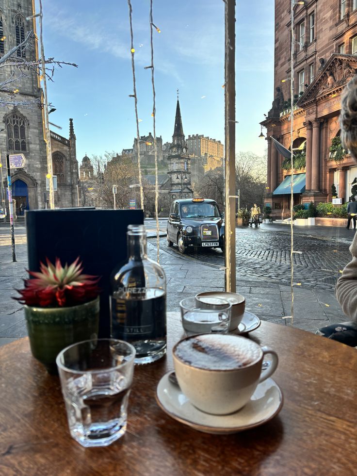 Café table with coffee cups and water glasses overlooking Edinburgh street with church spires and black cab