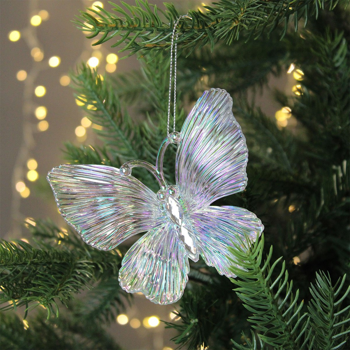 Translucent butterfly ornament with rainbow sheen hanging on evergreen Christmas tree with twinkling lights