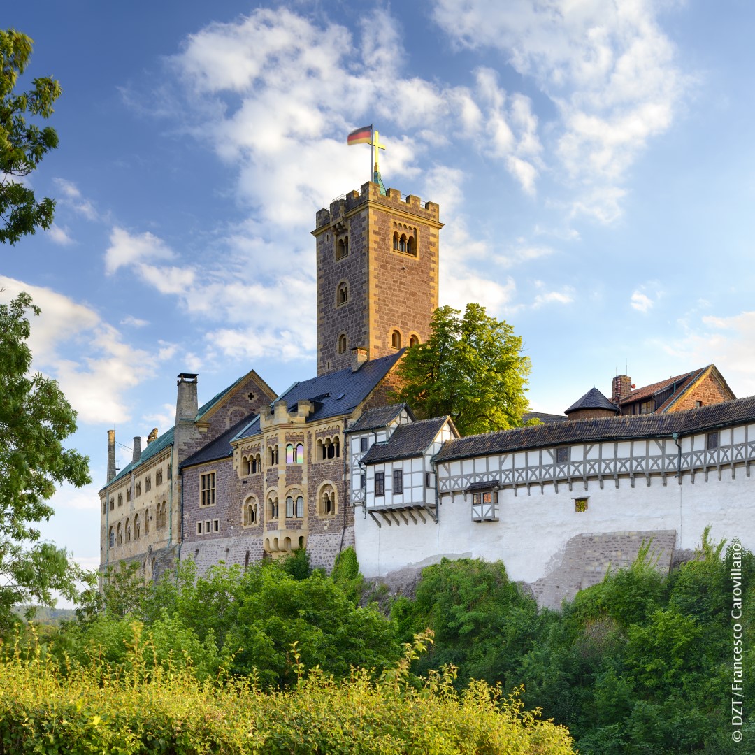 Medieval Wartburg Castle with stone tower and half-timbered buildings on forested hill against blue sky with clouds