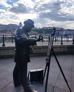 Bronze statue of artist with easel overlooking Budapest waterfront under cloudy sky