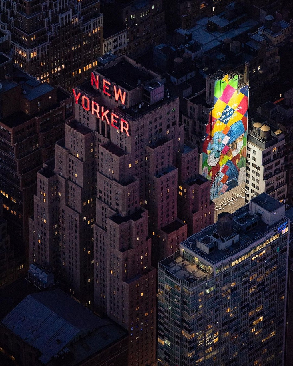 Aerial view of the New Yorker Hotel at dusk with illuminated red sign and colorful building mural