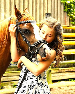 Young girl in floral dress hugging brown pony outdoors
