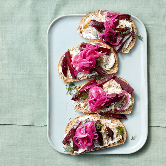 Four open sandwiches topped with trout, beets and pink pickled onions on a white plate