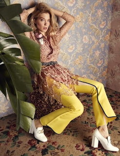 Woman in patterned dress and yellow pants posing against decorative floral wallpaper