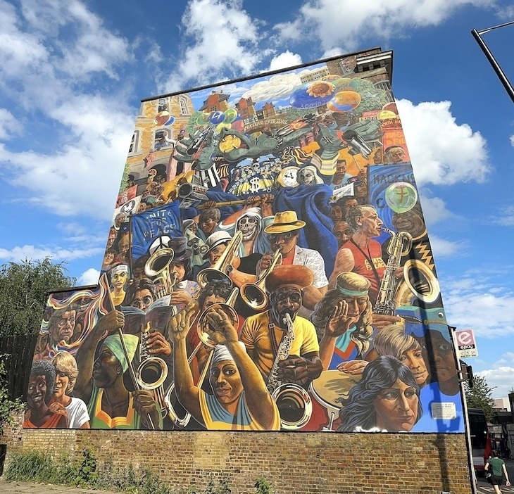 Large colorful mural on brick building showing crowd of people in carnival celebration with musicians and festive scene