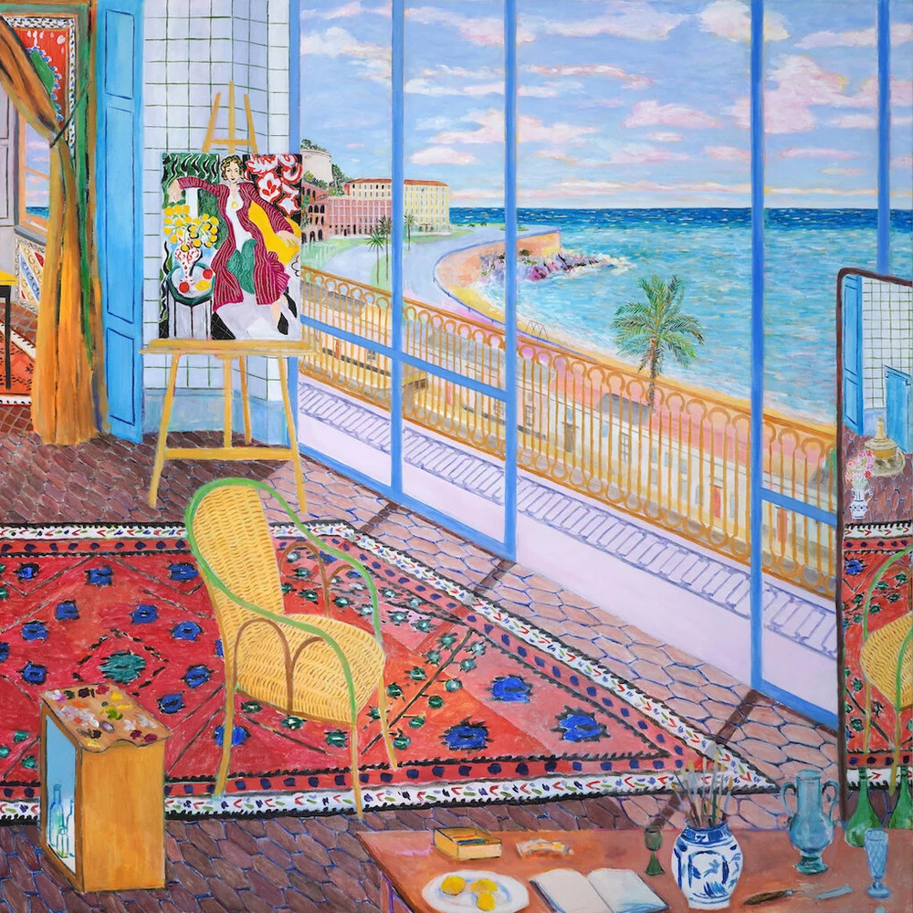 Bright artist studio with ocean view through large windows, easel with artwork, patterned rug and yellow wicker chair